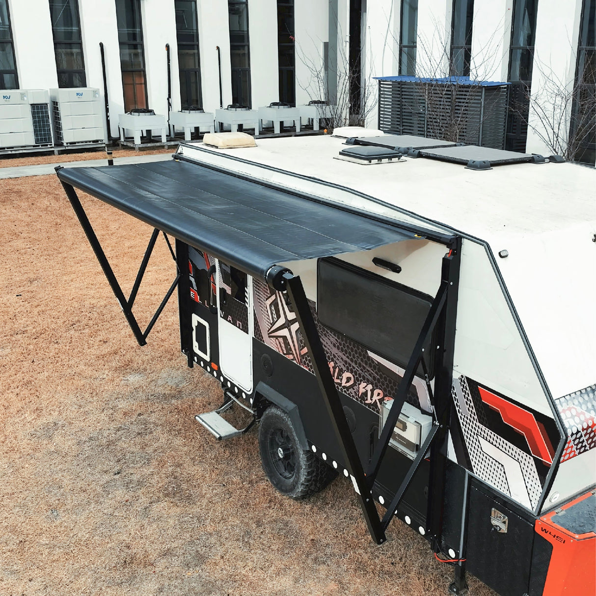 AWNLUX electric solar RV awning fully extended on off-road camper trailer, showing reinforced support arms and black solar fabric